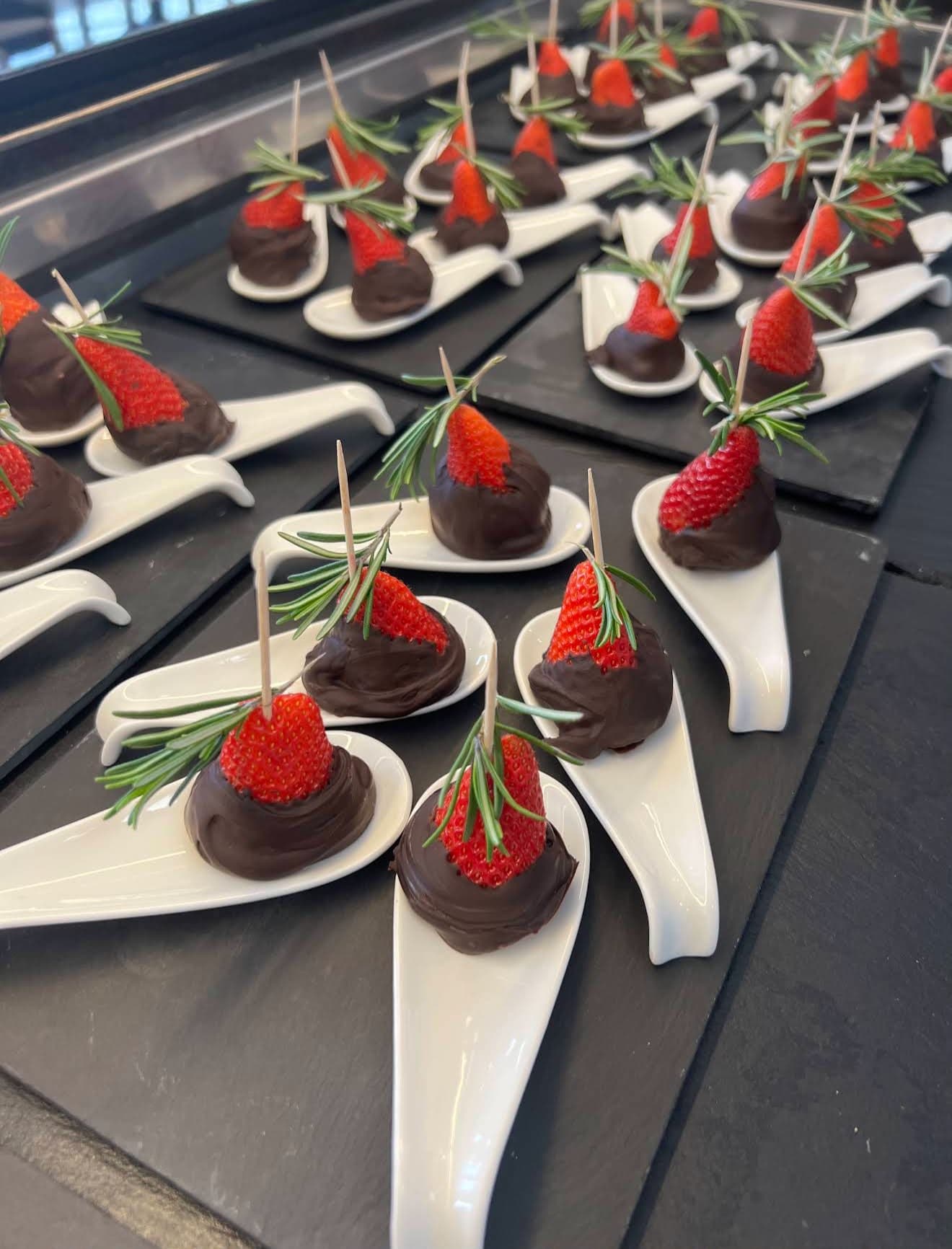 Schokolierte Erdbeeren mit Rosmarin auf weißen Löffeln
