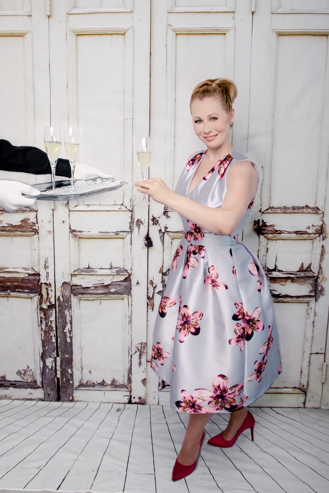Nadine im Blütenkleid nimmt lachend ein Glas Champagner vom Tablett